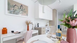 Eine moderne Küche mit weißen Schränken, ein Essbereich mit einem weißen Tisch für zwei Personen und ein Kranenbild an der Wand.