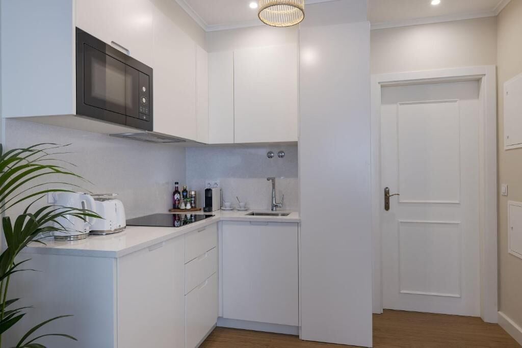 A compact kitchen with white cabinetry, a microwave, a sink, and a door leading to another room.