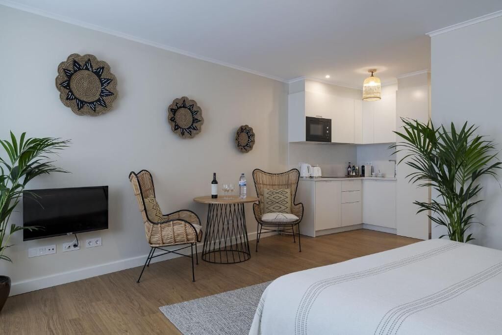 A compact room with a bed, a TV, a dining area with chairs, a small kitchen, and wall decorations.