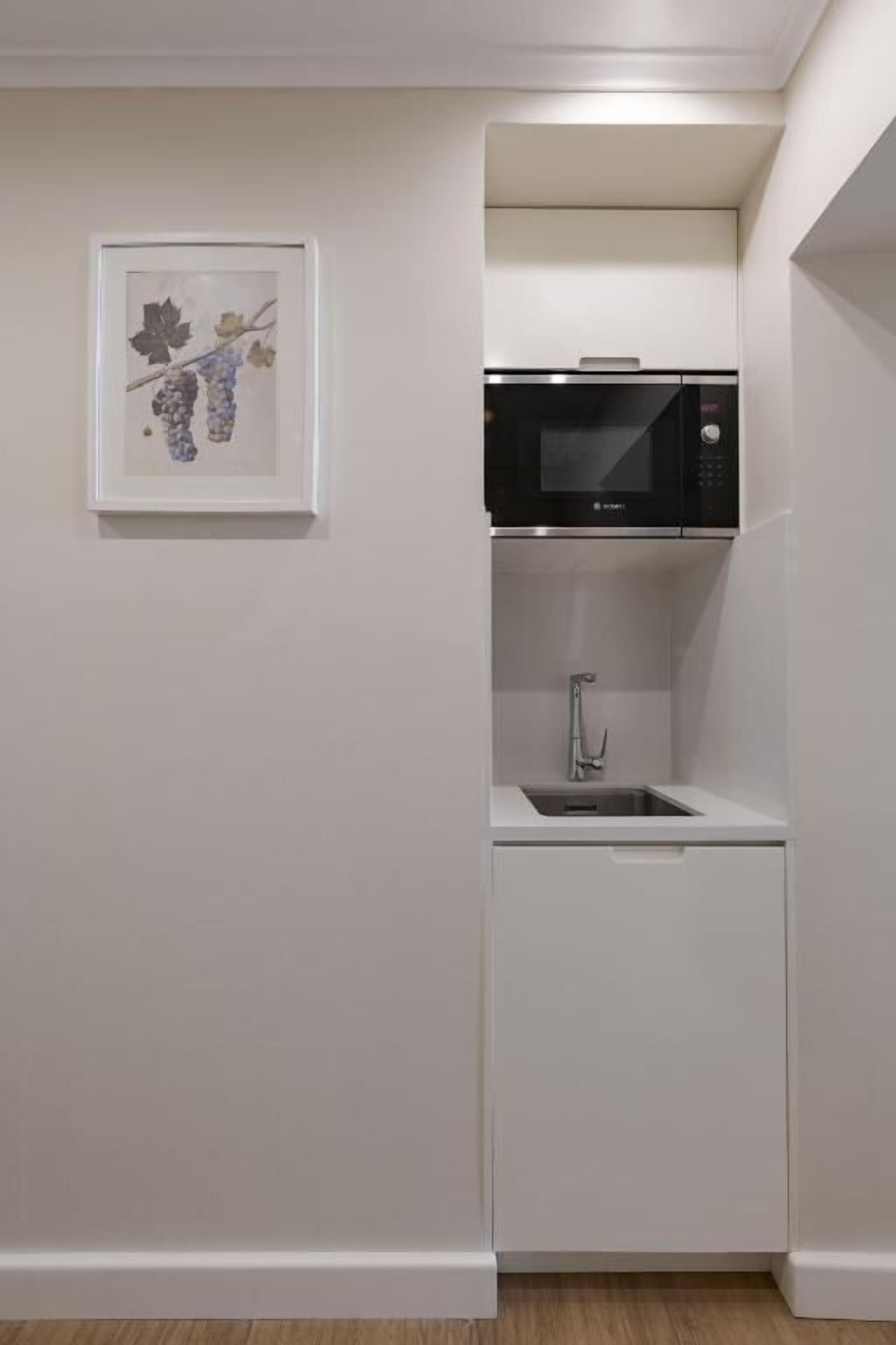 A compact kitchenette with a microwave, sink, and a framed artwork on the wall.