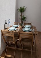 Mesa de madera para cuatro personas, dispuesta con platos, cubiertos y vasos, junto a una botella de vino y una de agua.
