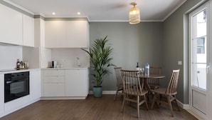 Une cuisine moderne avec des meubles blancs, un four encastré, une table à manger avec des chaises en bois et une plante en pot.