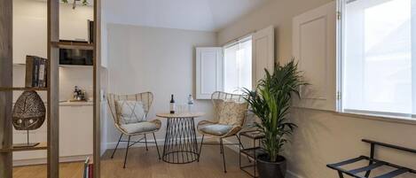 Un salon moderne avec un plancher en bois, deux fauteuils en osier, une petite table ronde, une plante en pot et une bibliothèque.