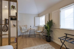 Un salon moderne avec un plancher en bois, deux fauteuils en osier, une petite table ronde, une plante en pot et une bibliothèque.