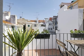 Un balcon agrémenté d’un pot de fleurs, d’un banc en bois et offrant une vue sur les bâtiments voisins.