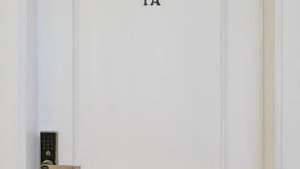 Une porte blanche portant le numéro 1A, un système de verrouillage à clavier et un plancher en bois.