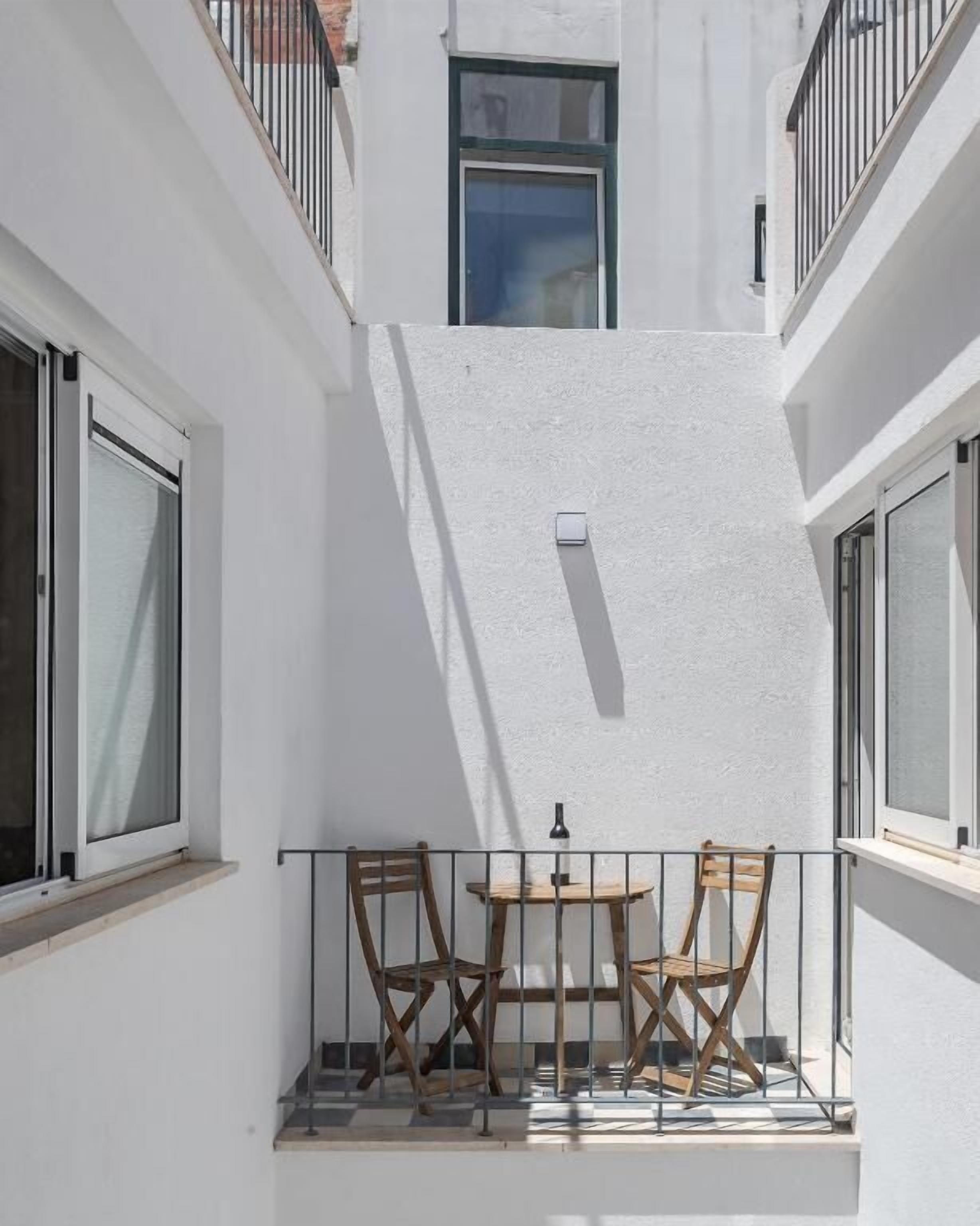 Ein kleiner Balkon mit zwei Holzstühlen und einem Tisch, weißen Wänden und einem Fenster.