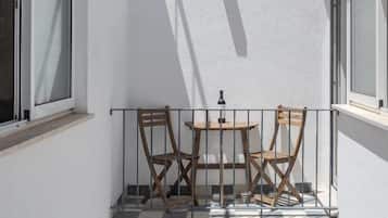 Ein kleiner Balkon mit zwei Holzstühlen und einem Tisch, weißen Wänden und einem Fenster.