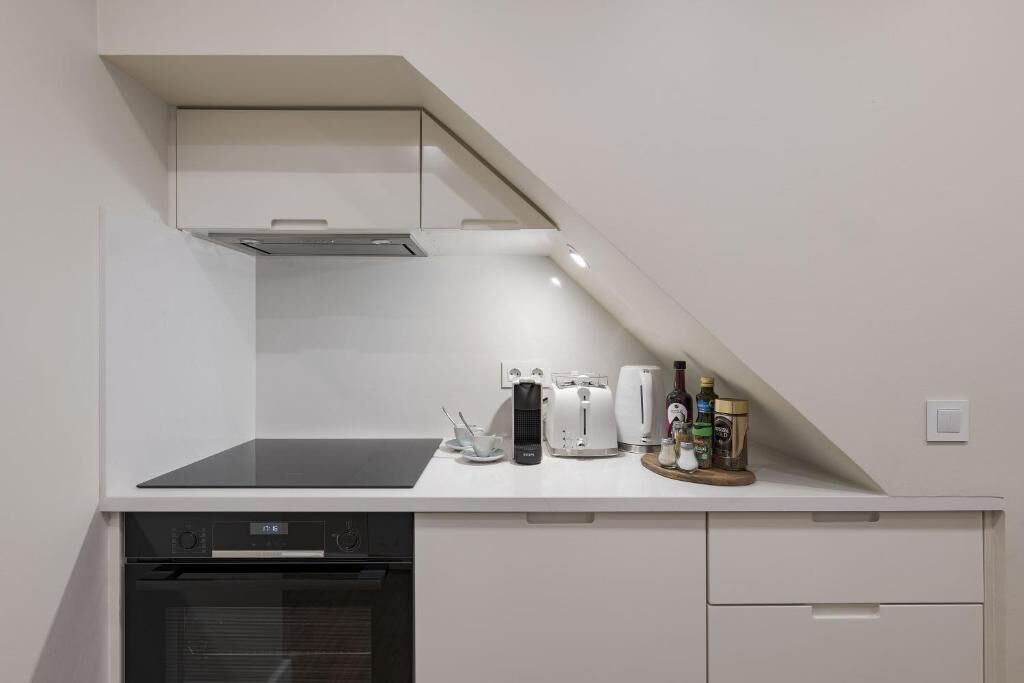 Uma cozinha compacta com forno embutido, cafeteira, torradeira e um pequeno balcão com diversos utensílios de cozinha.