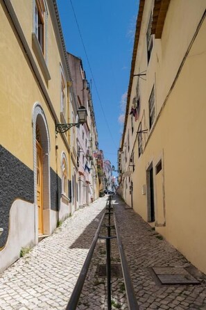 A narrow cobblestone street flanked by buildings with arched doorways and windows, leading to a distant view. - Peixeira Studios and Apartments (Lisbon)