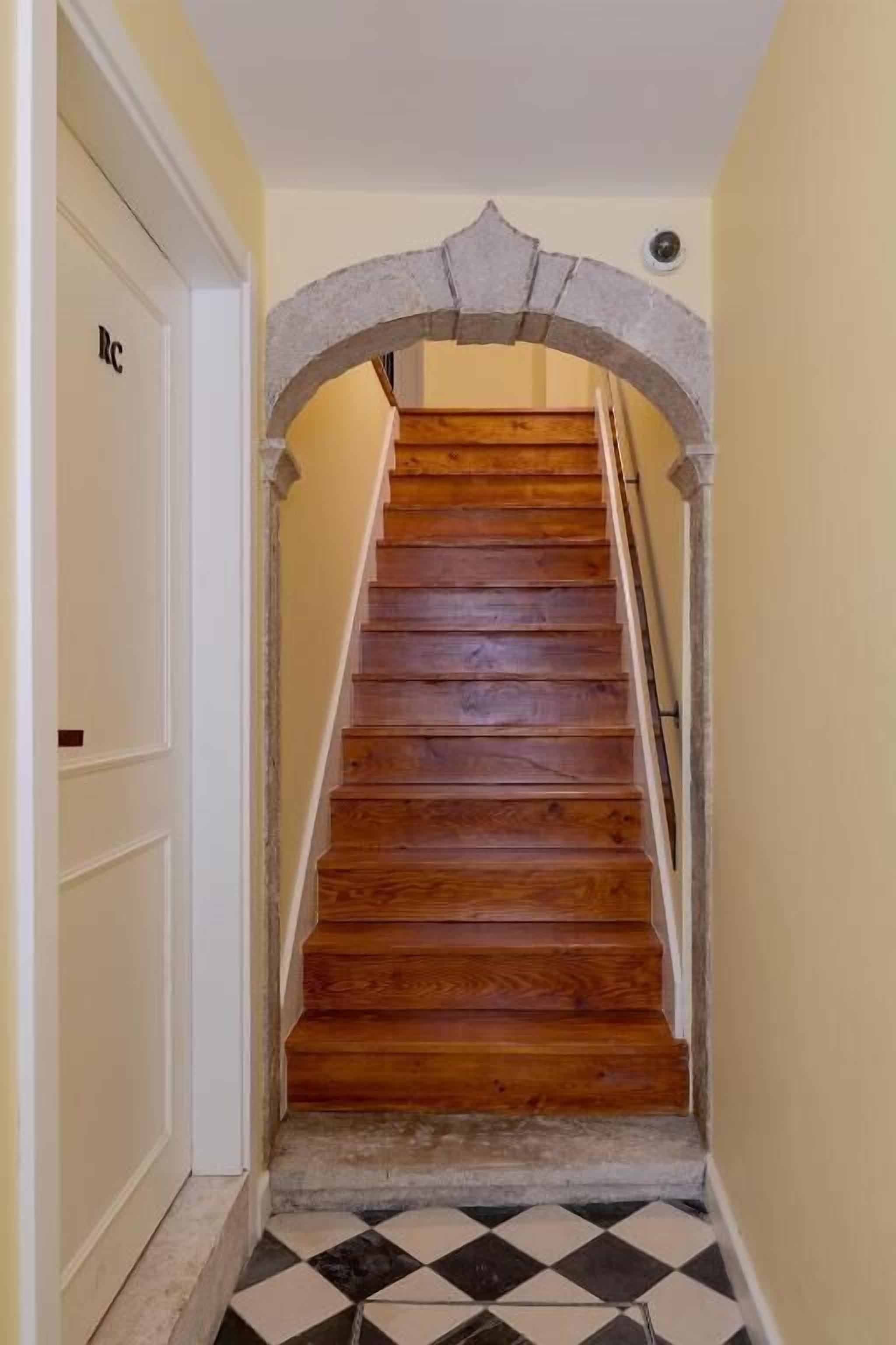 A wooden staircase with a stone archway, leading to a room with a white door marked "RC".
