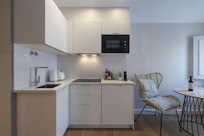 A compact kitchen with white cabinetry, a microwave, a kettle, and a wicker chair. - Peixeira Studios and Apartments (Lisbon)