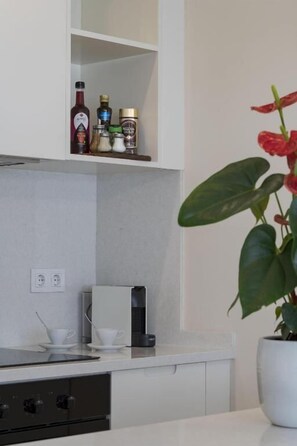 Una cocina moderna con encimera blanca, una cafetera y una planta en maceta.