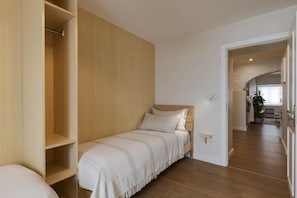 A bedroom with a single bed, a wooden wardrobe, and a view of a dining area. - Peixeira Studios and Apartments (Lisbon)