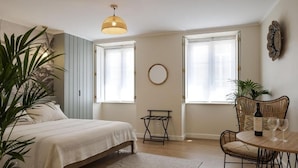Une chambre à coucher avec un lit, une table avec des verres à vin, une chaise, un luminaire suspendu et un miroir rond accroché au mur.