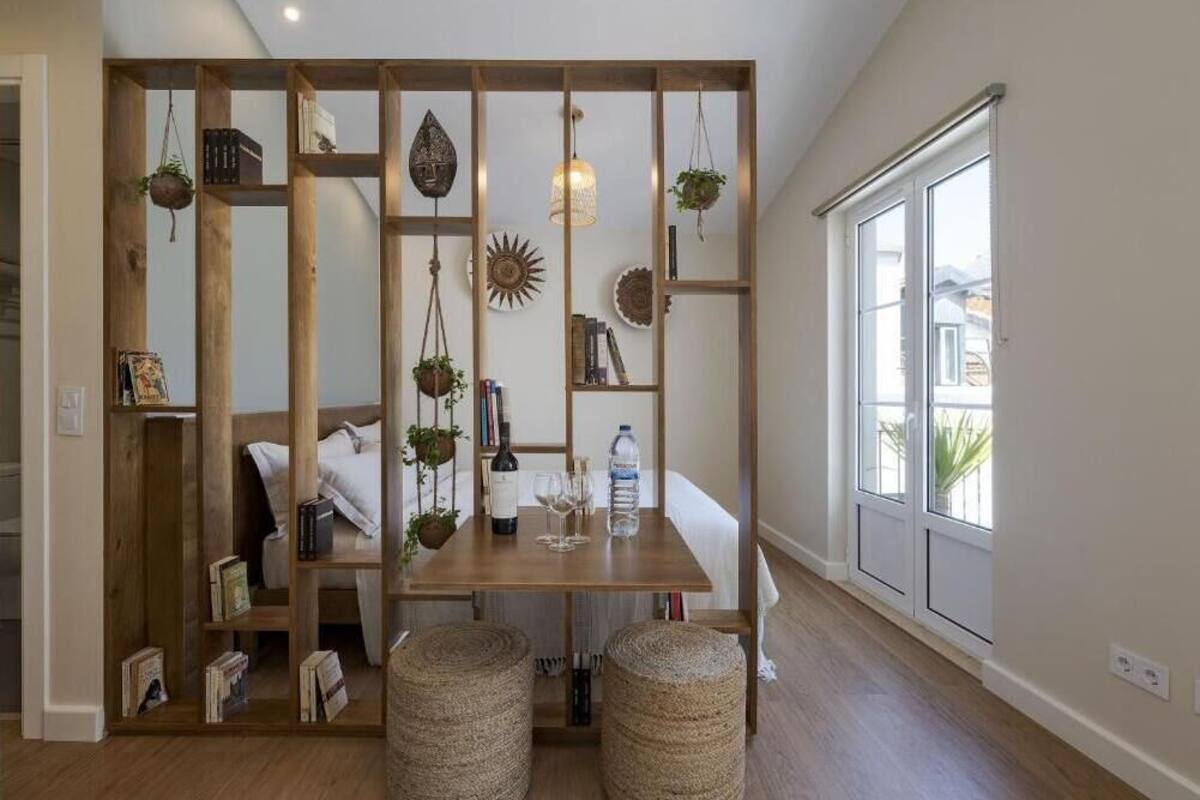Une pièce avec un séparateur en bois, une table à manger avec une bouteille et des verres, et une grande fenêtre.