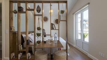 Um quarto com um separador de madeira, uma mesa de jantar com uma garrafa e copos, e uma janela grande.