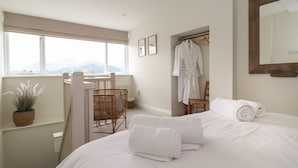 Ein Schlafzimmer mit einem großen Bett, einem Fenster mit Blick, einem Sessel, einem Bademantel und einem Spiegel.