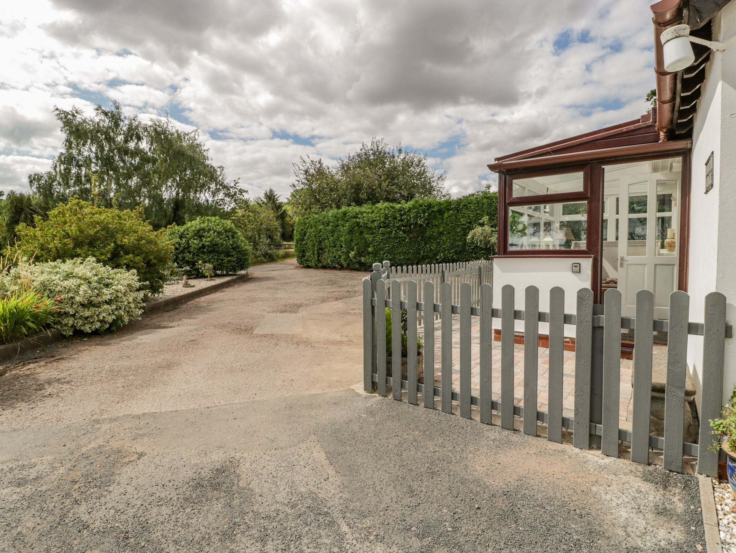 A gravel driveway leading to a white house with a wooden fence.