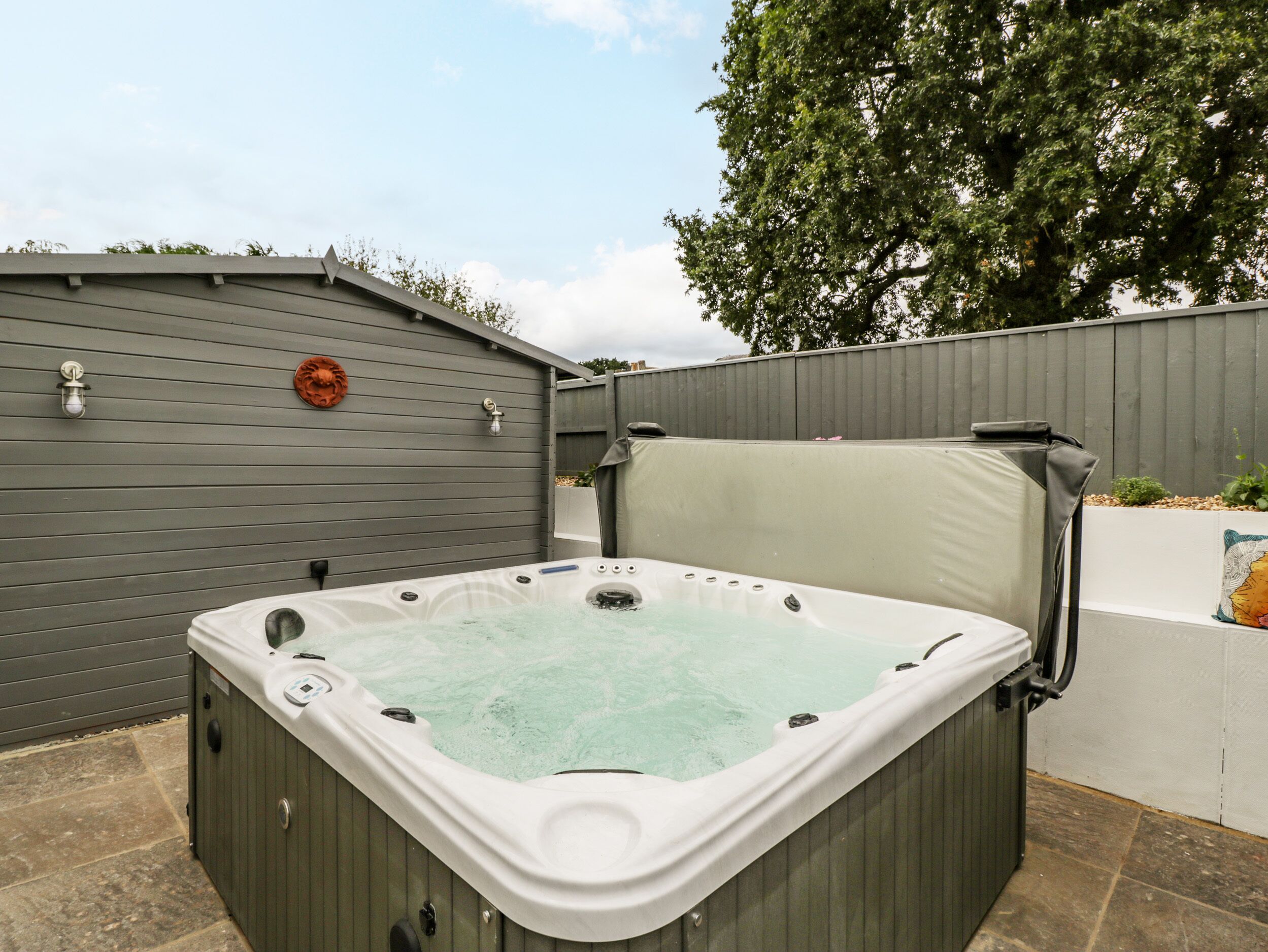 A hot tub in an outdoor setting with a grey fence and a tree in the background.