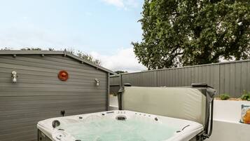 A hot tub in an outdoor setting with a grey fence and a tree in the background.