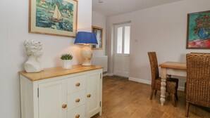 Una habitación con un armario blanco, una mesa, sillas de mimbre y cuadros en las paredes.