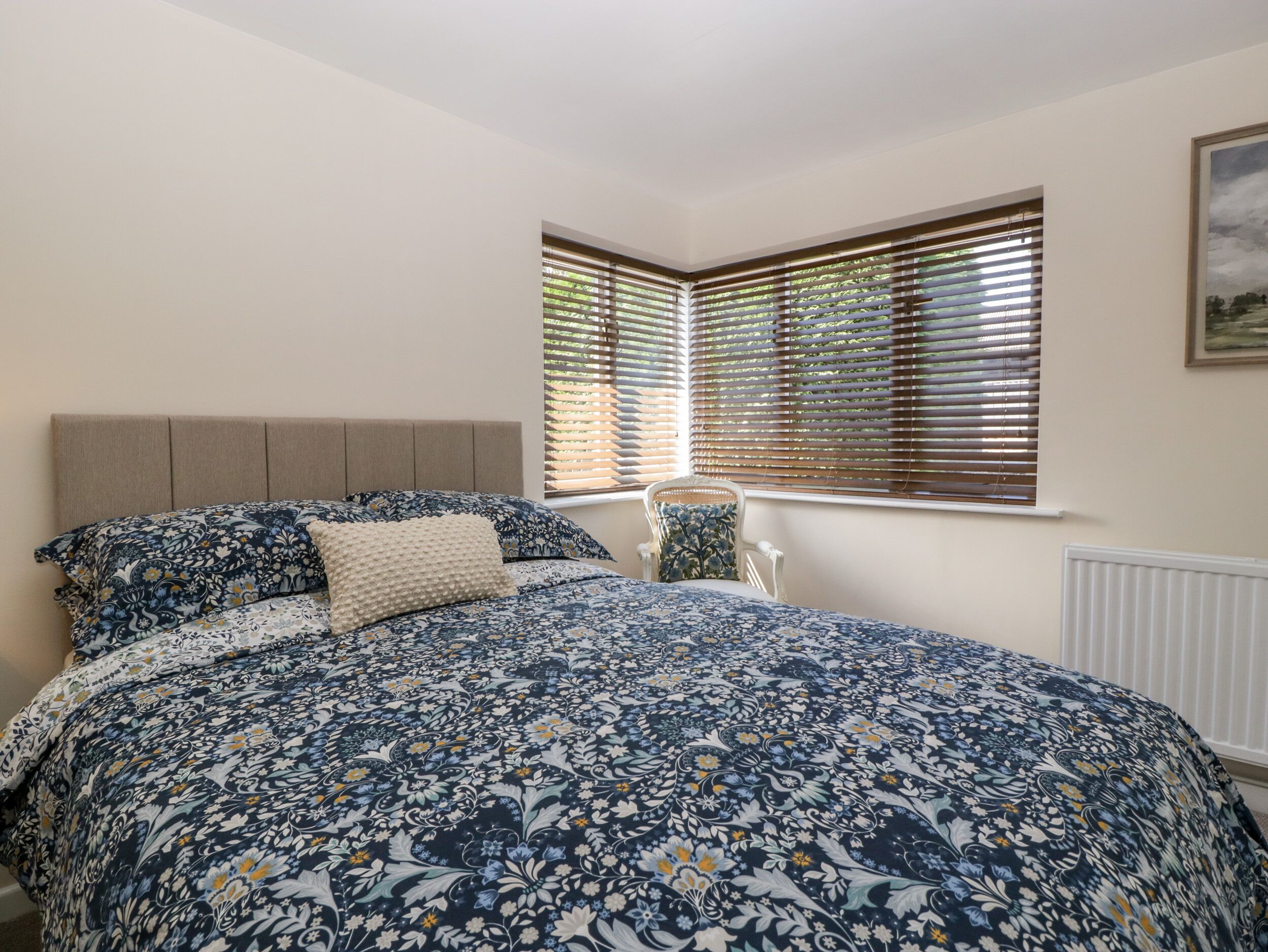 Un dormitorio con una cama grande, una silla y dos ventanas con persianas.