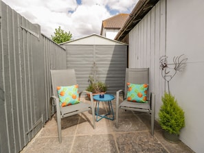 A patio with two chairs and a small table, surrounded by a grey fence and a white wall.