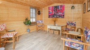 Interior acogedor de una cabaña de madera con techo de madera, una mesa de comedor, dos sillas, una planta pequeña y un cuadro abstracto y colorido en la pared.