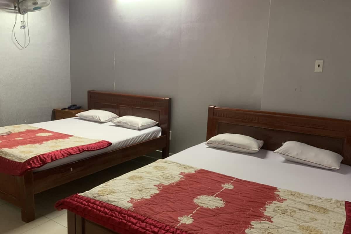 Two wooden beds with white and red bedding, a bedside table, and a wall-mounted fan.