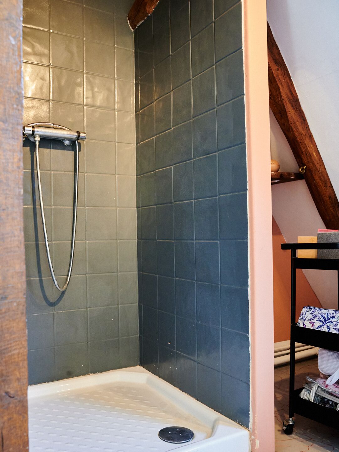 A shower area with dark blue tiles, a handheld showerhead, and a white bathtub with a drain.