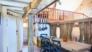 A rustic wooden dining area with a wooden table and chairs, a stone wall, and a wooden staircase.