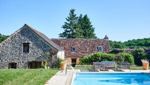 Ein Steingebäude mit Pool, umgeben von Grünpflanzen und blauem Himmel.