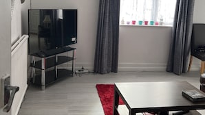 A modern living room with a flat-screen TV, a red rug, and a dining table.