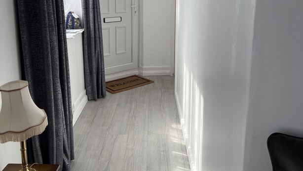 A hallway with a white door, a doormat, a lamp, and a bench.