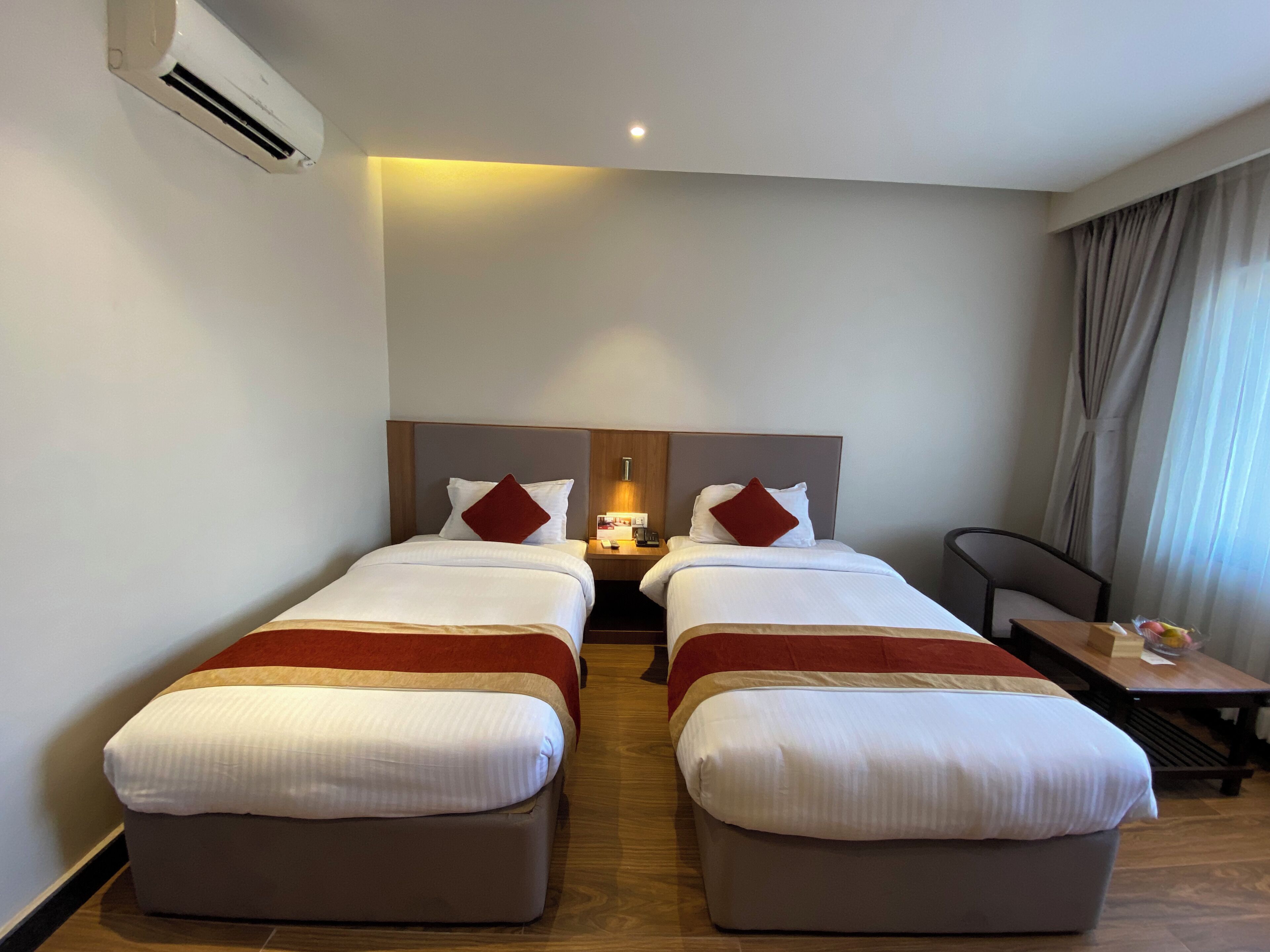 Habitación de hotel con dos camas, una mesita de noche, un escritorio, un equipo de aire acondicionado y vistas al exterior.