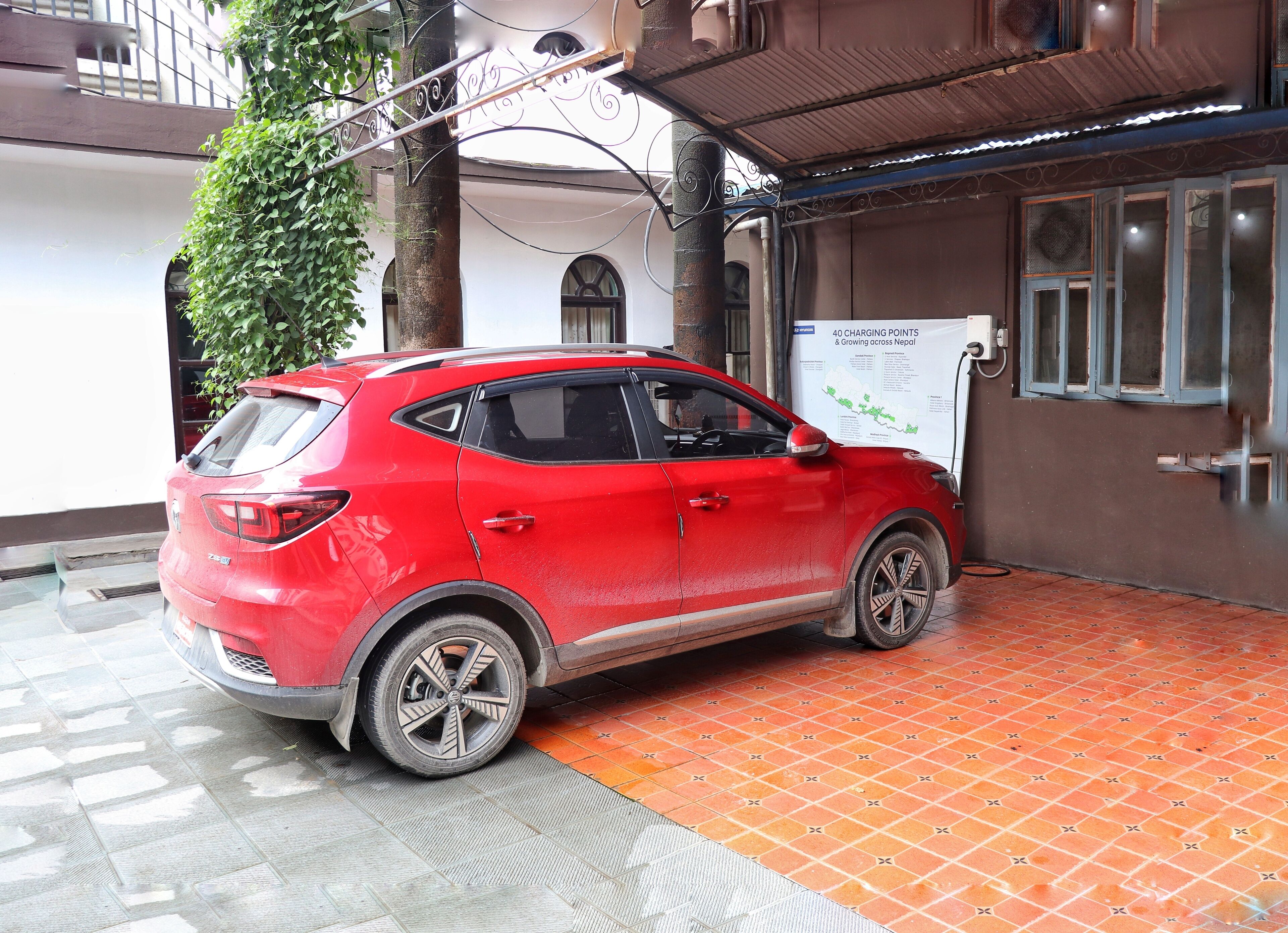 A red car parked in front of a building with a sign that reads "40 CHARGING POINTS & Growing across Nepal".