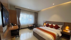 Quarto de hotel com cama grande, escrivaninha, cadeira, televisão e janela com cortinas.