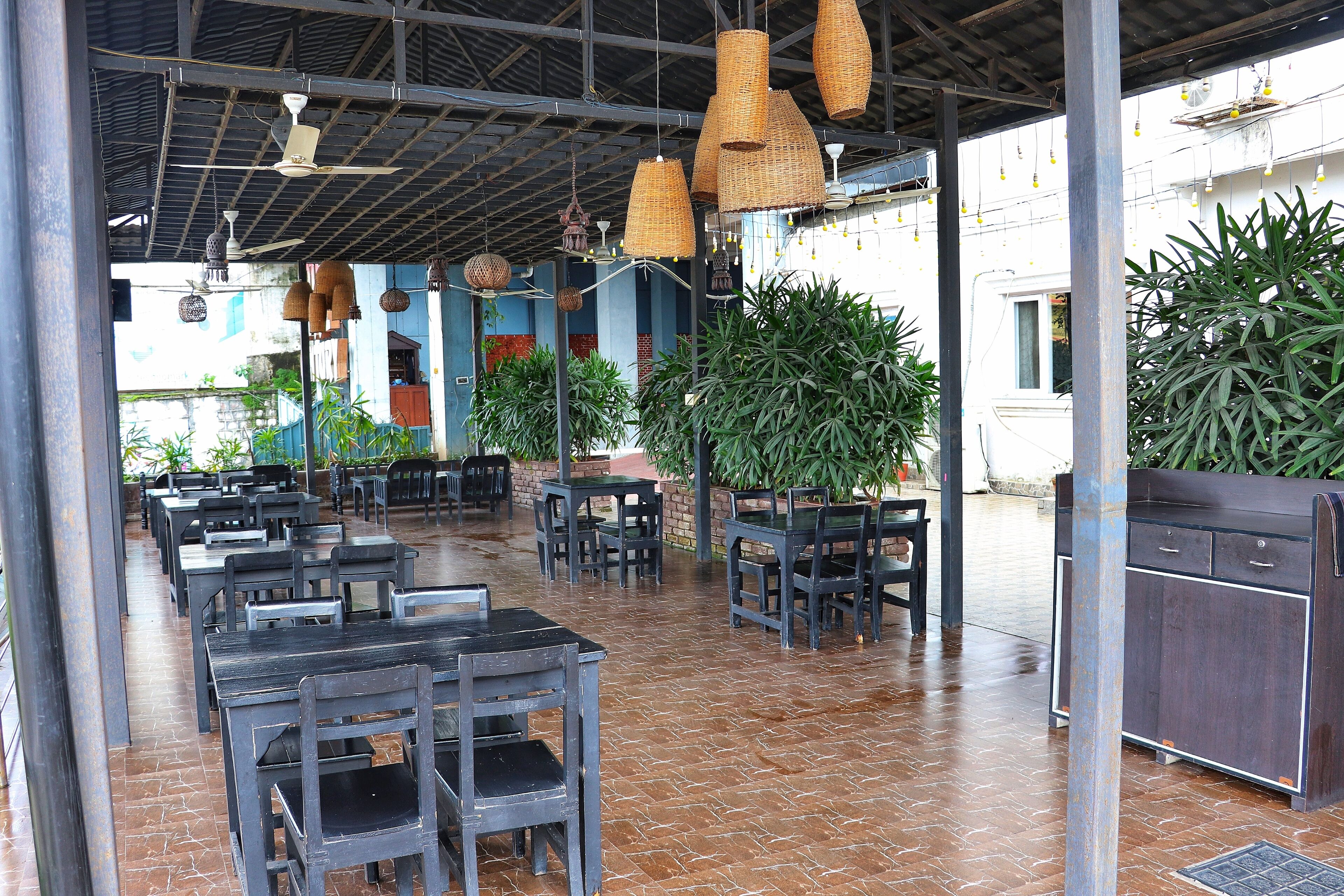 An outdoor dining area with tables and chairs, ceiling fans, hanging light fixtures, and potted plants.