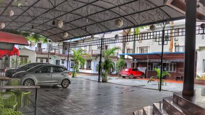 Uma área externa coberta com piso de azulejos, guarda-corpo de metal e plantas em vasos.