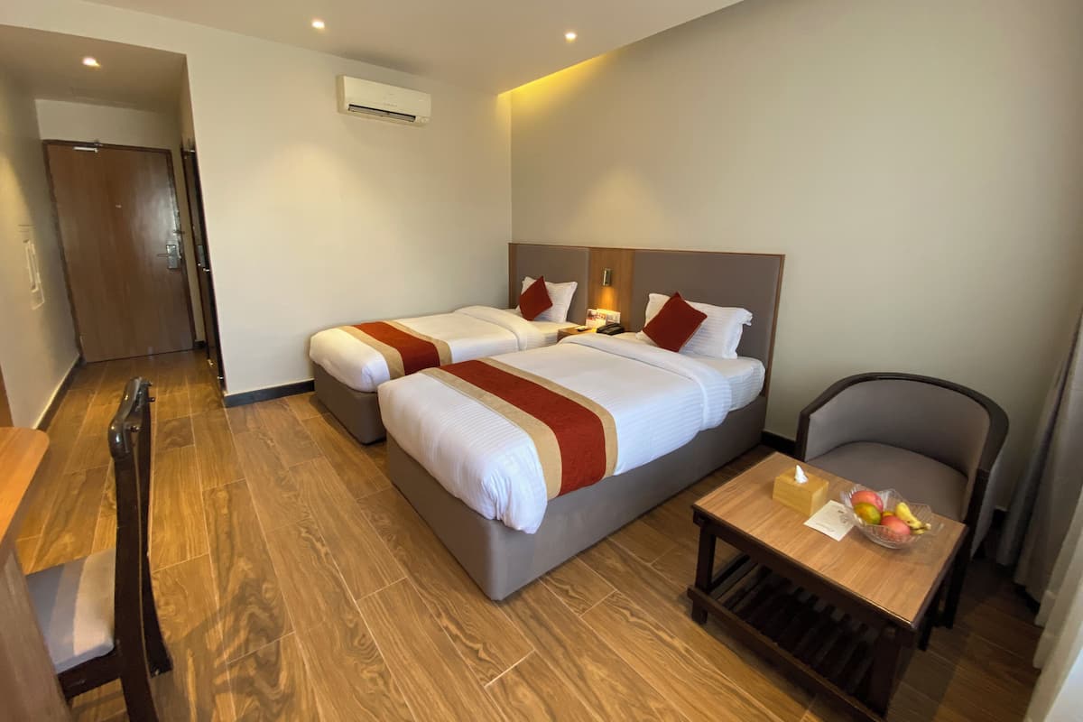 Une chambre d’hôtel avec deux lits, un bureau, une chaise et un appareil de climatisation.