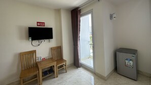 A room with a TV mounted on the wall, a wooden table with chairs, a refrigerator, and a sliding glass door leading to an outdoor area. - Italy Hotel (Nam Nha Trang)