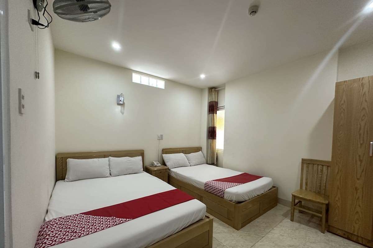 A hotel room with two single beds, a wooden wardrobe, a small wooden chair, and a window with curtains.