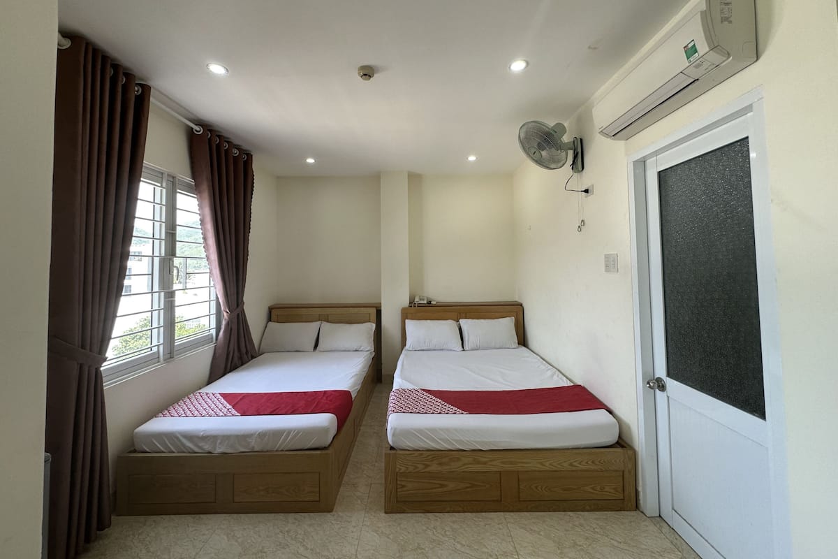A room with two beds, a window with curtains, an air conditioning unit, and a door.