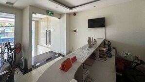 A reception area with a glass door, a flat-screen TV mounted on the wall, and a reception desk with a red folder. - Italy Hotel (Nam Nha Trang)
