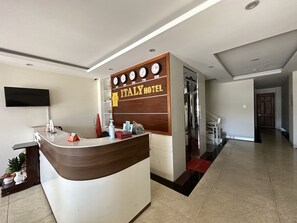 A reception desk with a wooden panel and a clock above it, labeled "ITALY HOTEL". - Italy Hotel (Nam Nha Trang)