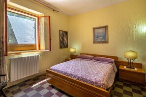Une chambre à coucher comprenant un lit, deux tables de chevet, une fenêtre avec des stores et deux lampes fixées au mur.