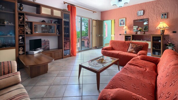 Een woonkamer met een bank, salontafel, televisie en planken met diverse spullen.