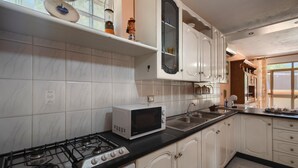 Een keuken met witte kastjes, een gasfornuis, een magnetron en een spoelbak.