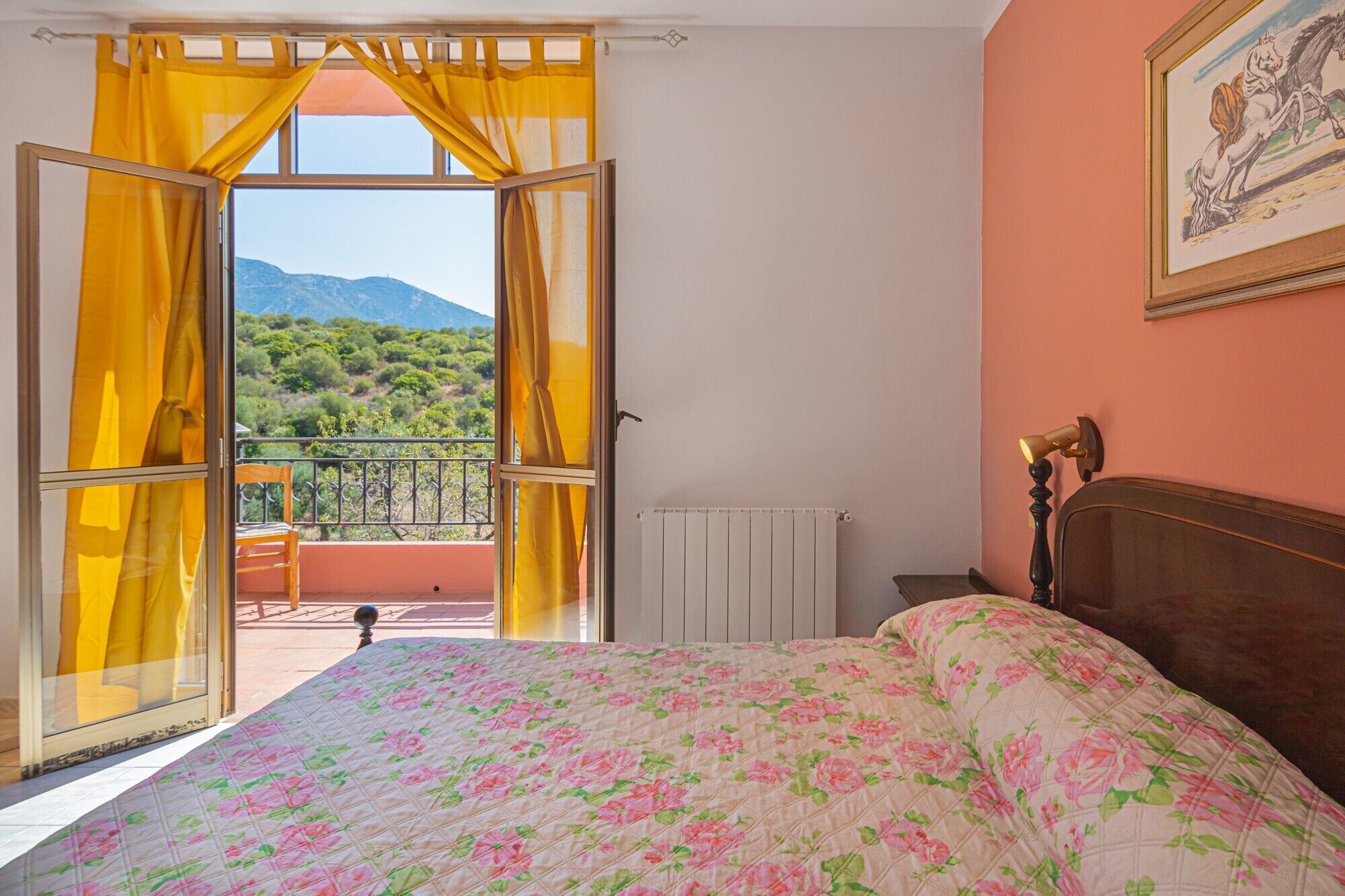 Een slaapkamer met een bed, een raam met gele gordijnen, een radiator en een ingelijste foto aan de muur.